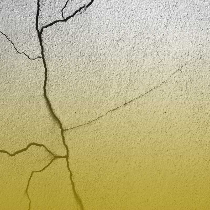 Zbliżenie faktury tynku z rozchodzącymi się pęknięciami; przejście z szarości u góry do żółtego u dołu.